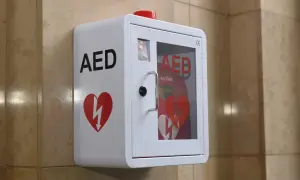 Biała szafka AED z czerwonym sercem i błyskawicą, zamontowana na ścianie.