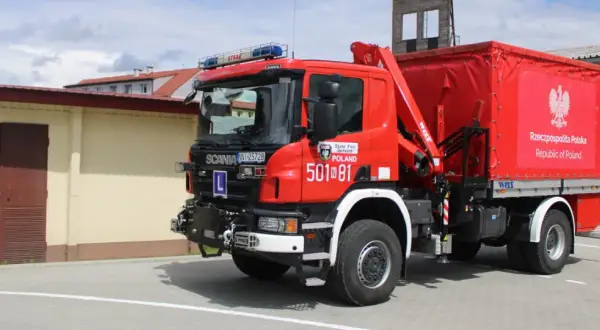 Czerwony strażak OSP Scania z żurawiem i plandeką z godłem Polski gotowy do akcji.