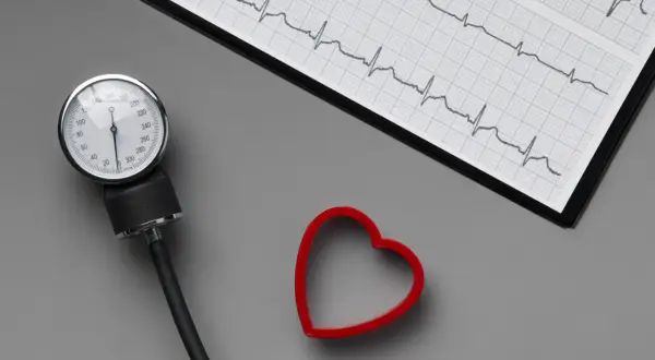 Ciśnieniomierz, EKG i czerwone serce na szarym tle.