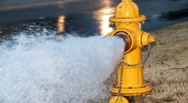 Żółty symbol hydrantu z łańcuchem, z którego tryska woda na mokrą ulicę.