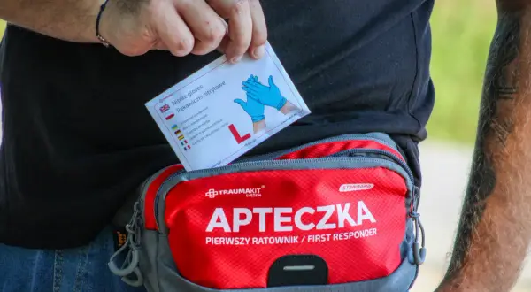 Dłoń wyjmuje z apteczki "Pierwszy ratownik" opakowanie rękawiczek nitrylowych.