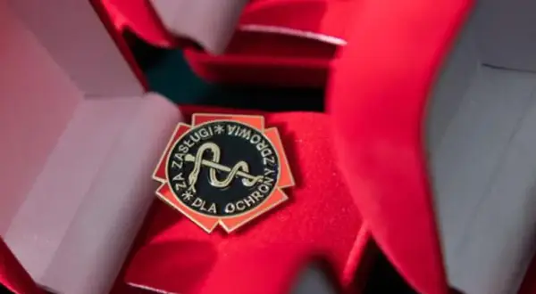 Odznaka "Za zasługi dla ochrony przeciwpożarowej" w otwartym, czerwonym pudełku.