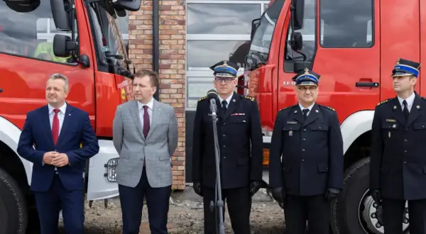 Uroczystość przed remizą OSP. W garniturach i mundurach strażackich stoją mężczyźni, wśród nich zastępca naczelnika OSP.