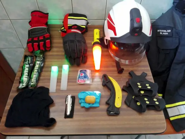 Na stole rozłożony sprzęt strażacki: rękawice, latarki, kask, nóż, raczki, kombinezon. Znajomość nazw sprzętu strażackiego jest kluczowa.